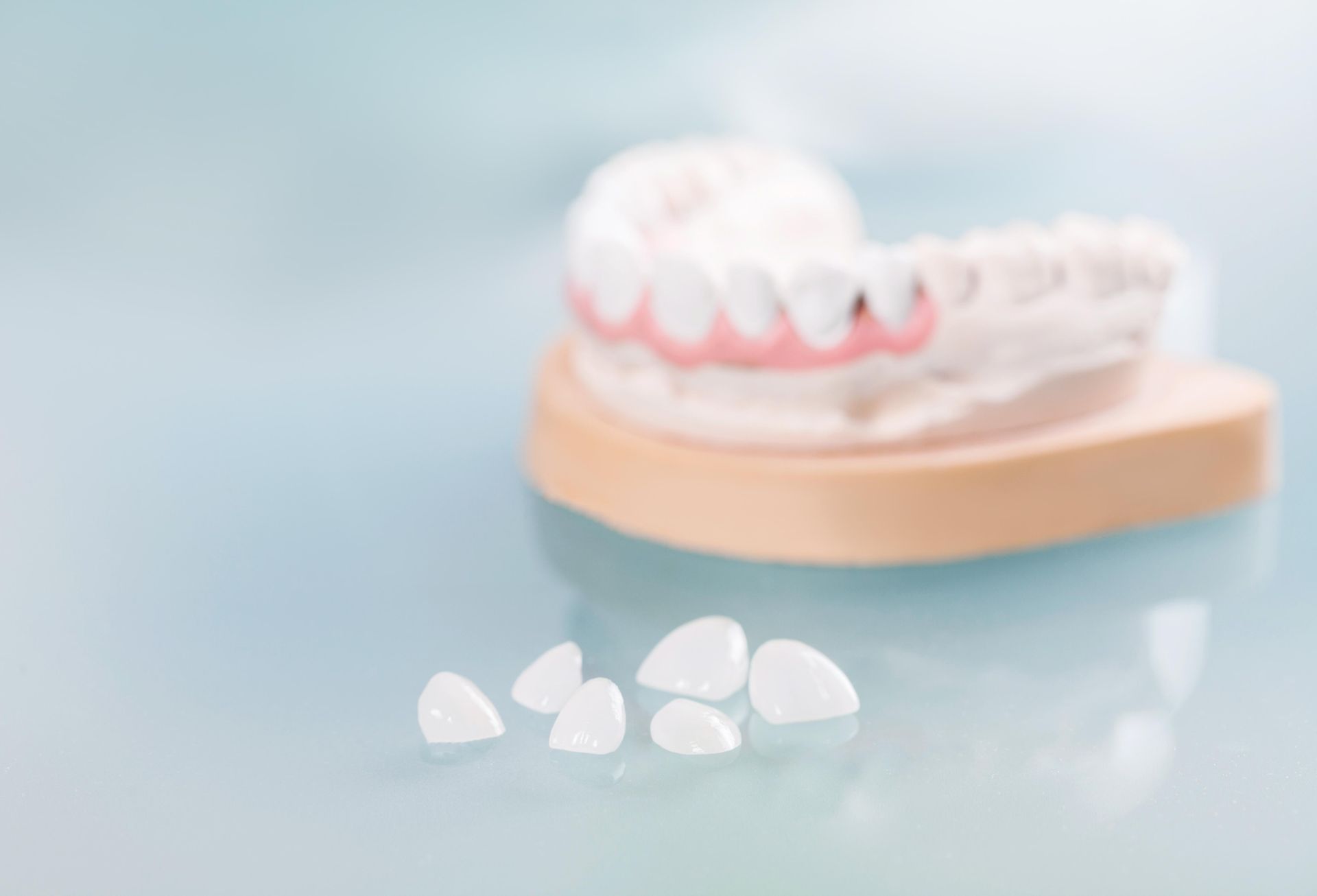 Dental model with white dentures and small white gum-shaped tablets on a pale blue surface