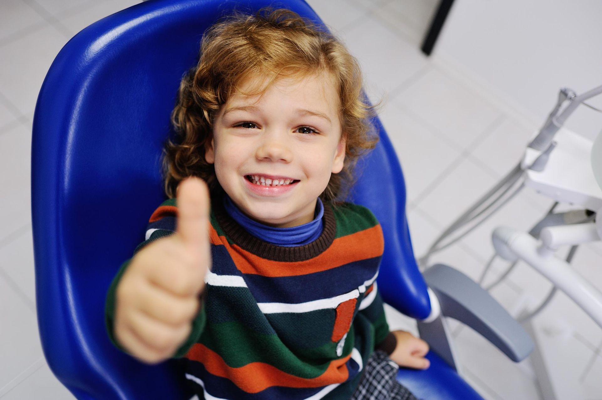 Smiling child in a blue dental chair giving a thumbs-up