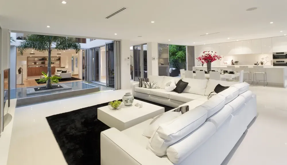 Modern white living room with a large sofa, black rug, and a central courtyard featuring a tree and reflecting pool. — George Pappas Painting In Buderim, QLD