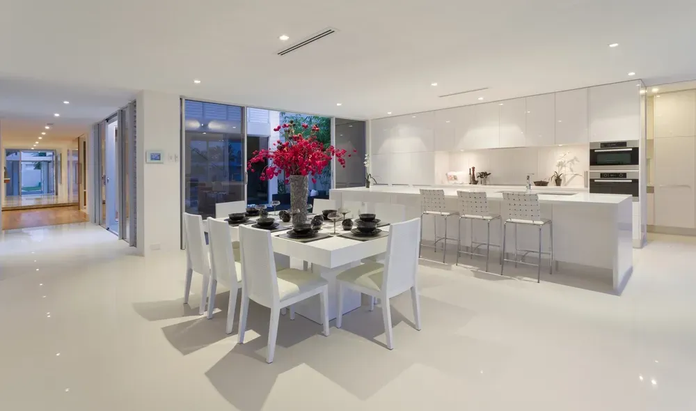 Modern, White Kitchen and Dining Area With a Long Table Set for Six and a Kitchen Island With Bar Stools — George Pappas Painting In Buderim, QLD