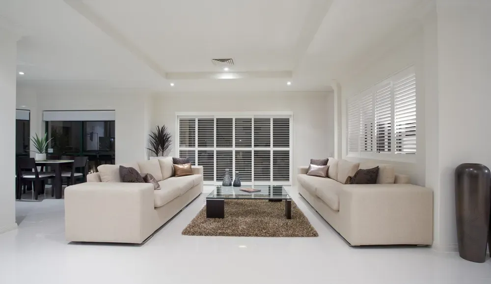 Bright modern living room with two beige sofas, large windows, and a central coffee table on a rug
