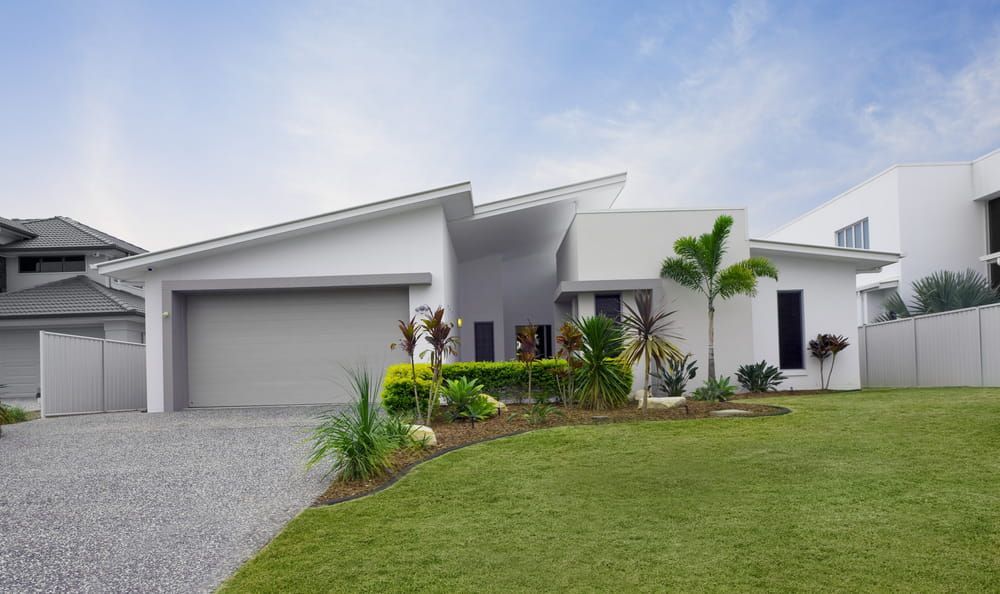 A modern, white single-story home with a split-pitched roof, a gravel driveway, and a well-maintained green lawn. — George Pappas Painting In Buderim, QLD
