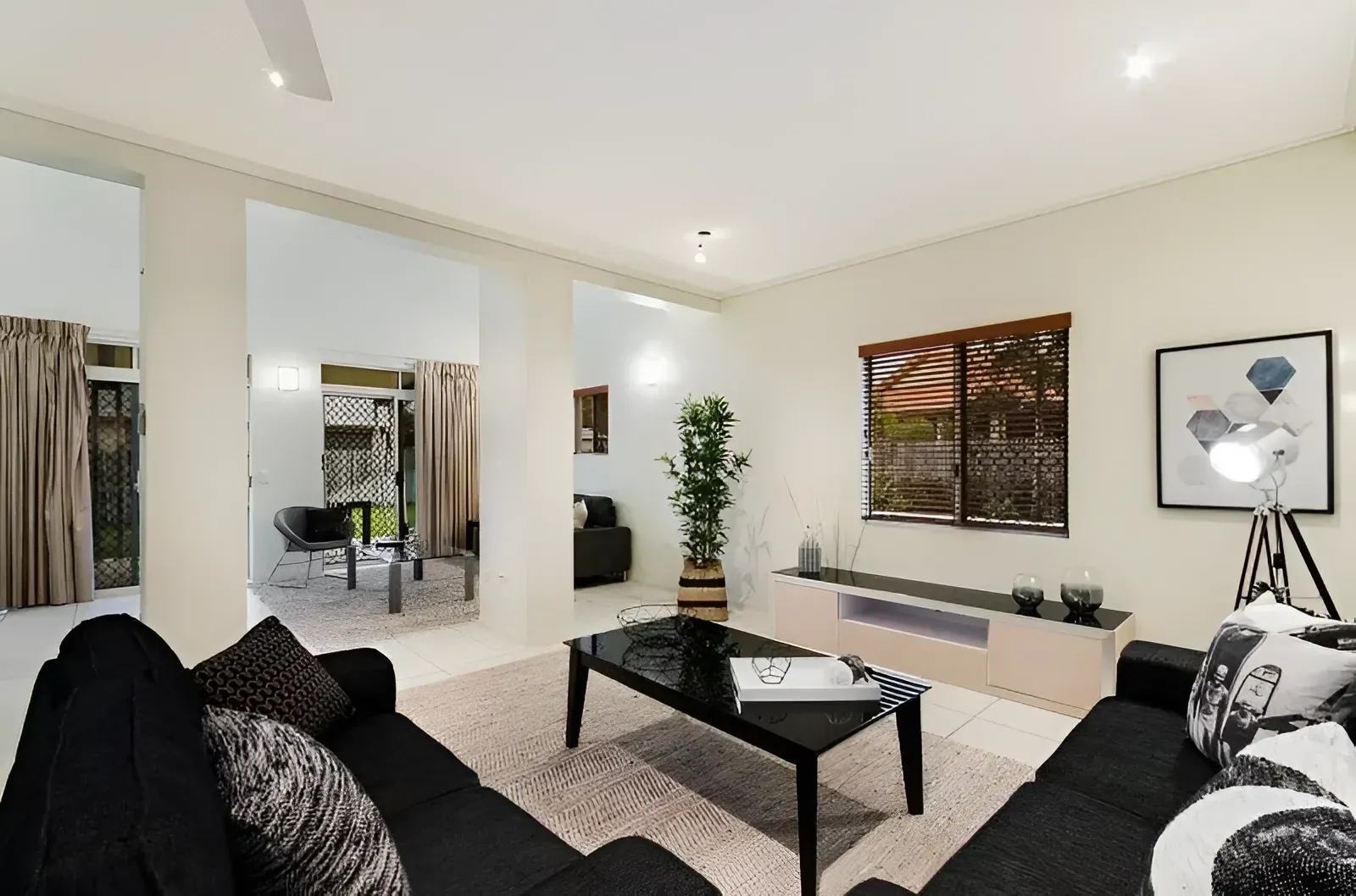 A modern living room with two black sofas, a black coffee table, a beige rug, and an open doorway to another room.