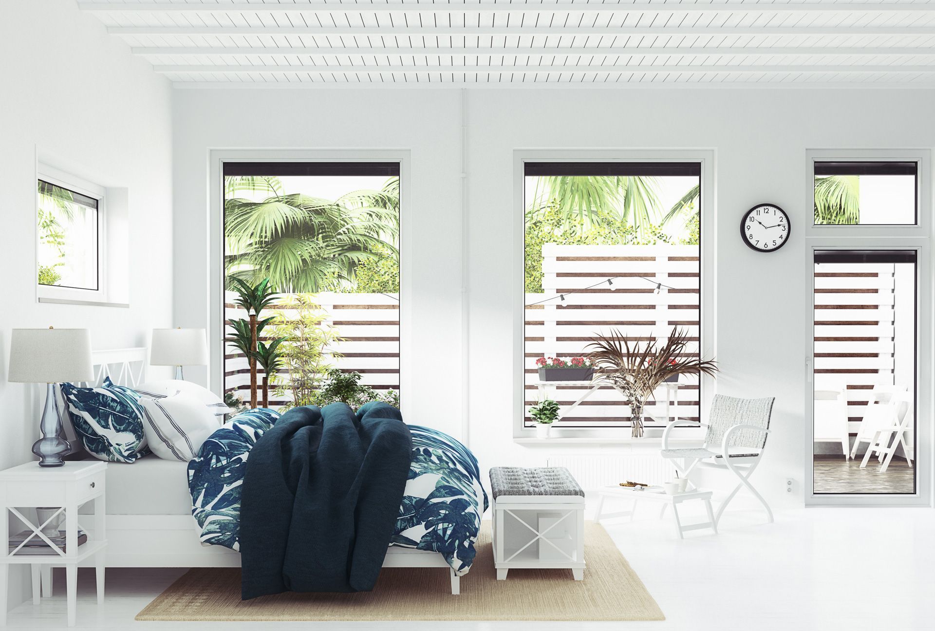 A bright, minimalist bedroom with white walls, a navy patterned bedspread, a bedside table, and large windows.