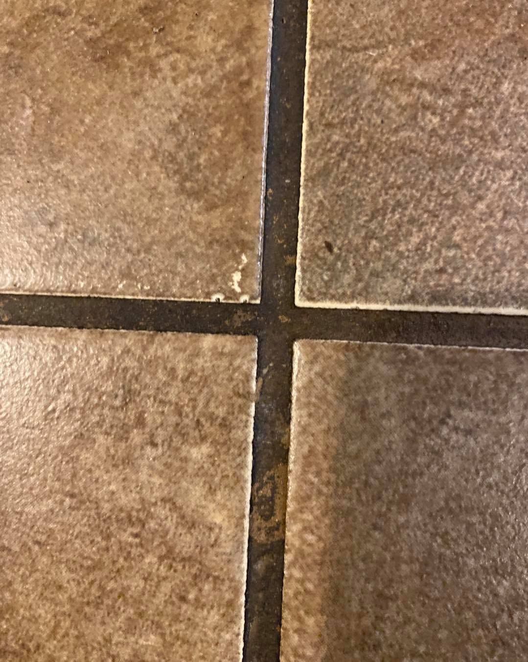 Close-up of brown stone floor tiles with dark grout lines forming a cross.