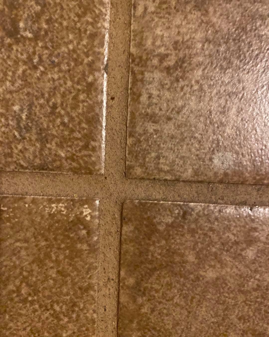 Close-up of brown, textured square tiles with grout lines forming a cross.