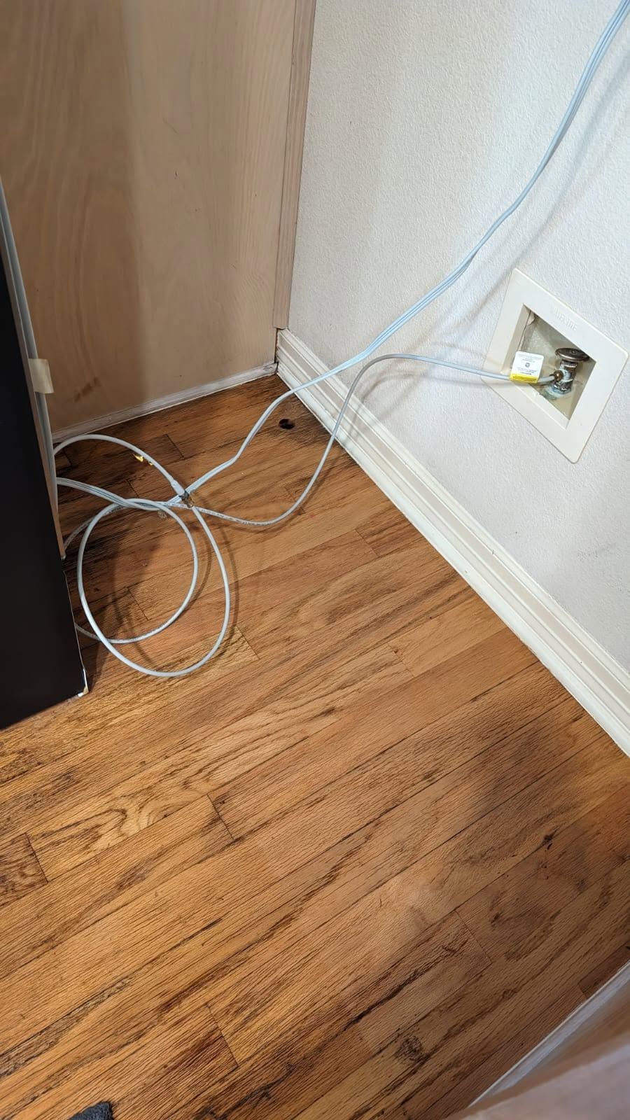 Loose white cables on a hardwood floor beside a wall outlet and wooden cabinet corner.