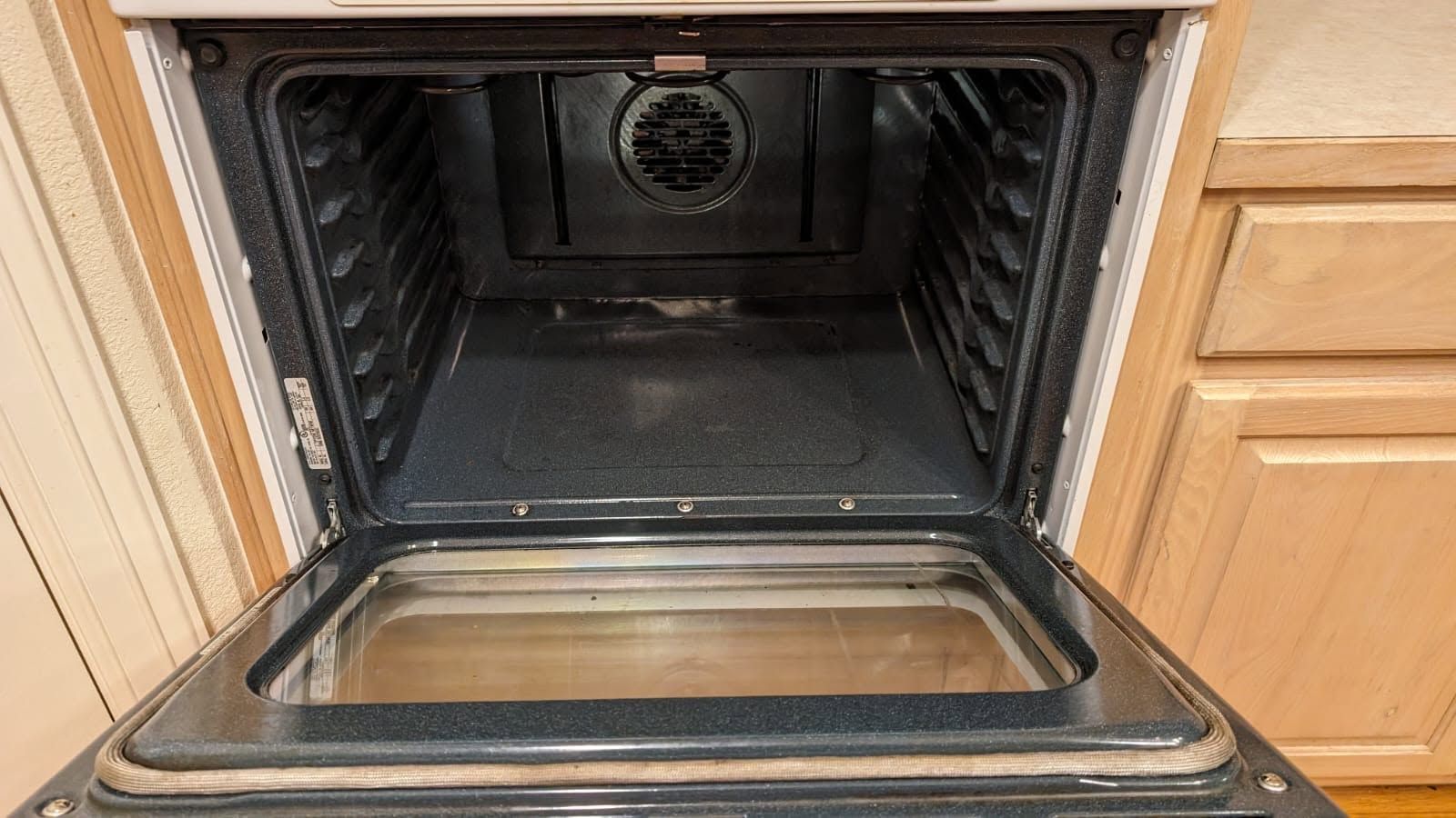 Open black oven with stainless steel interior in a kitchen cabinet.