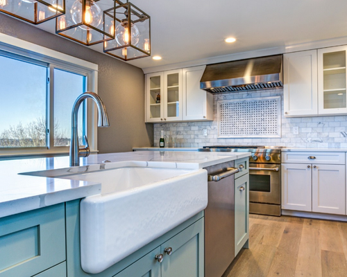 Modern kitchen with white cabinets, blue island, farmhouse sink, stainless appliances, and wood floors.