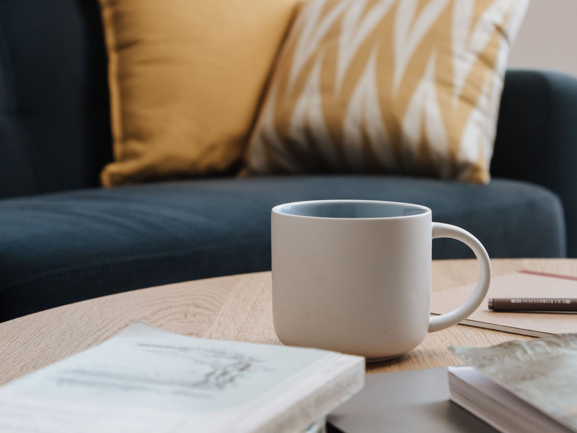 White mug on a wooden coffee table in front of a dark sofa with mustard and patterned cushions