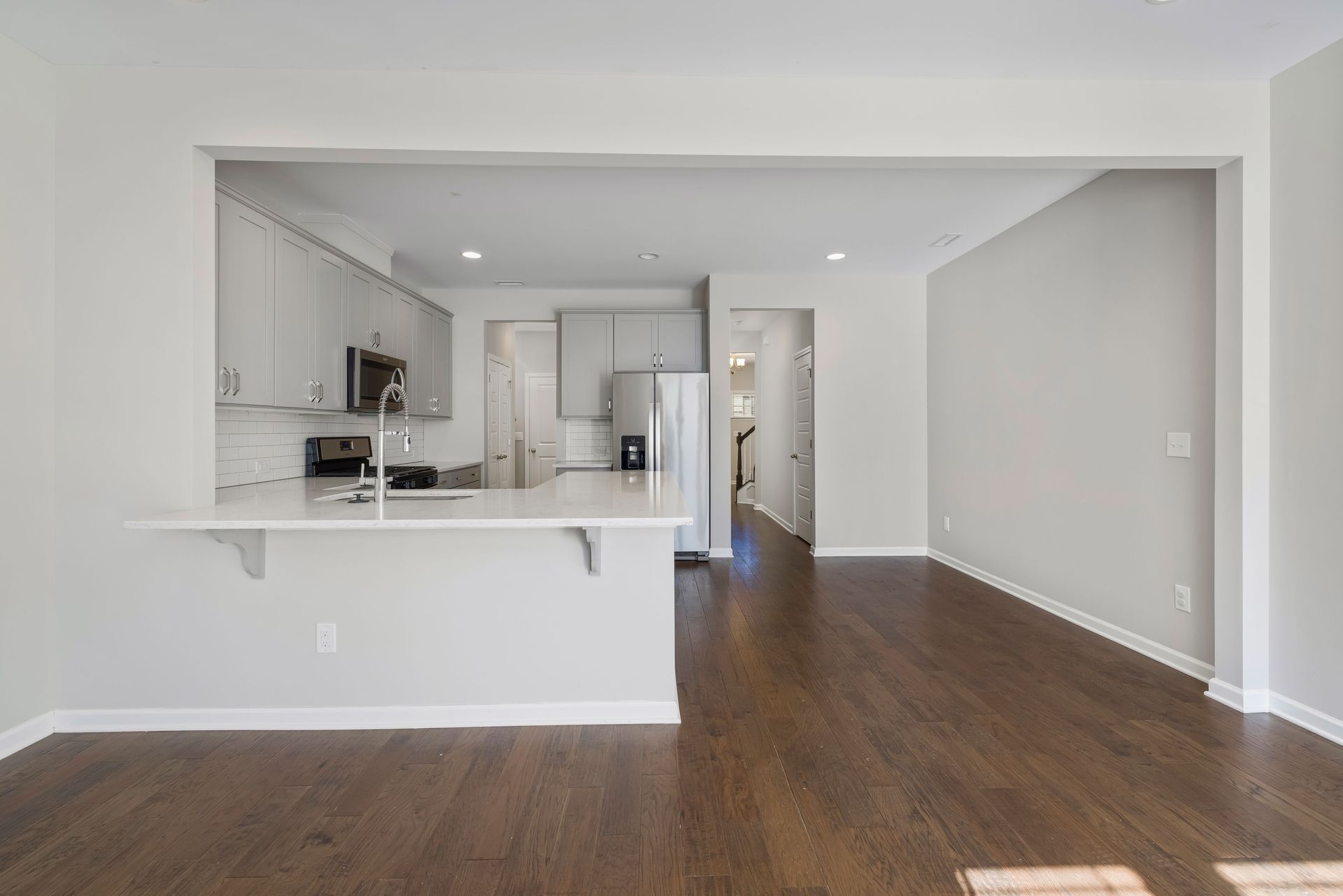 Empty modern apartment living area with open kitchen, white walls, and dark wood floors