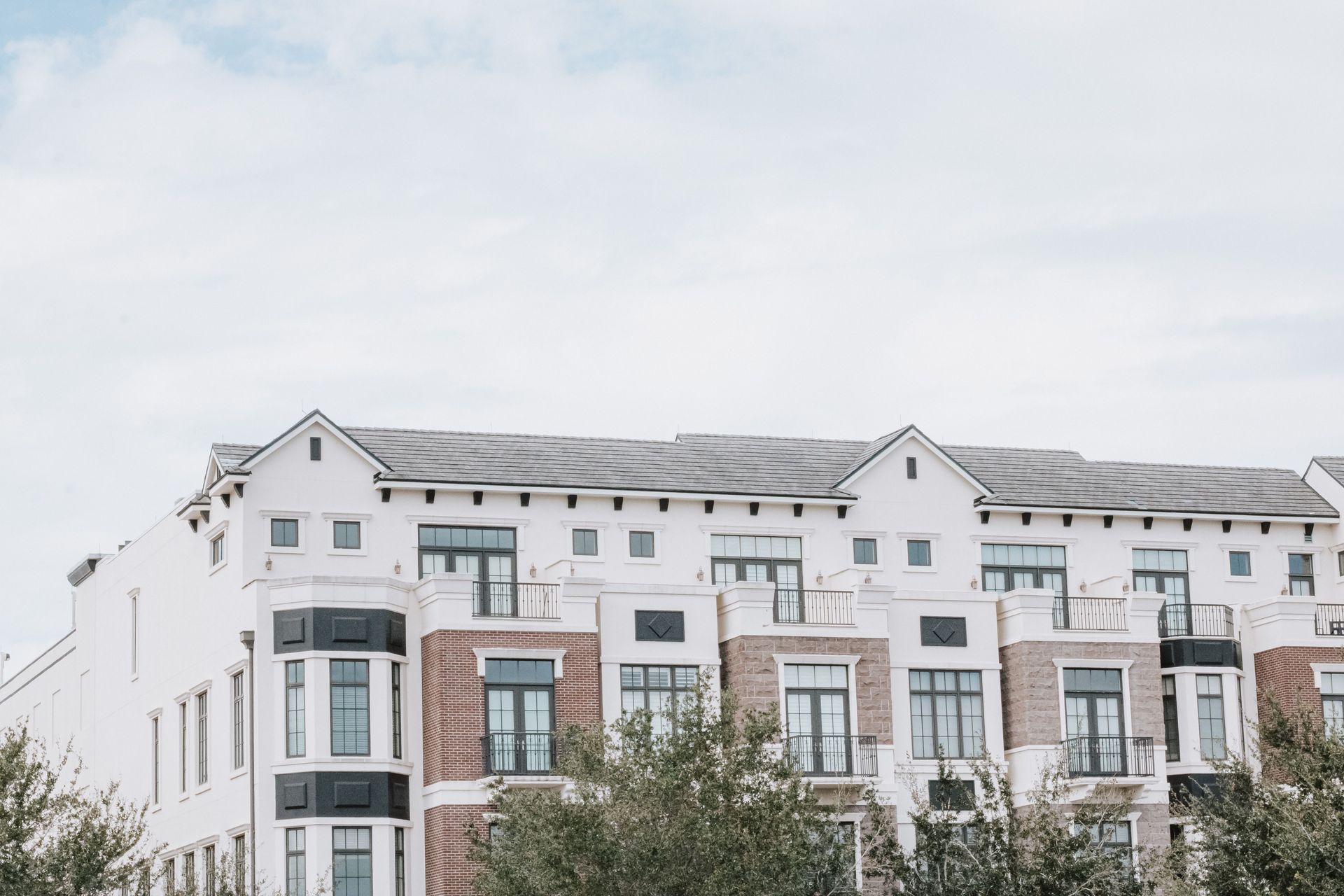 Modern white apartment building with balconies and a cloudy sky above