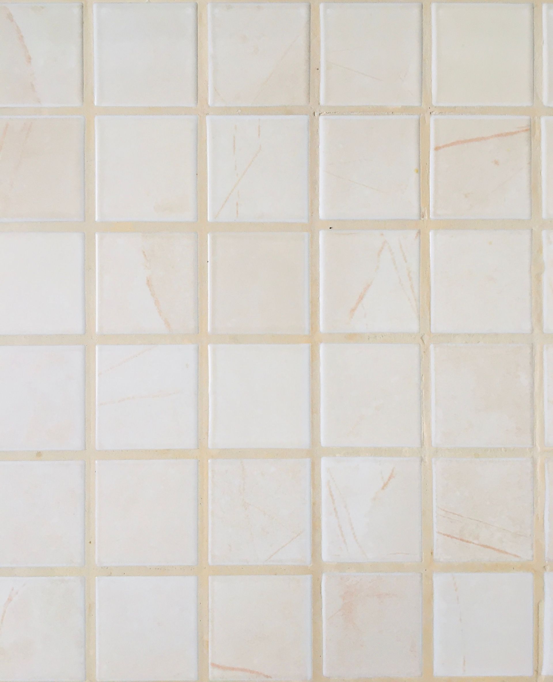 Beige tiled wall with a grid of square ceramic tiles and light grout lines