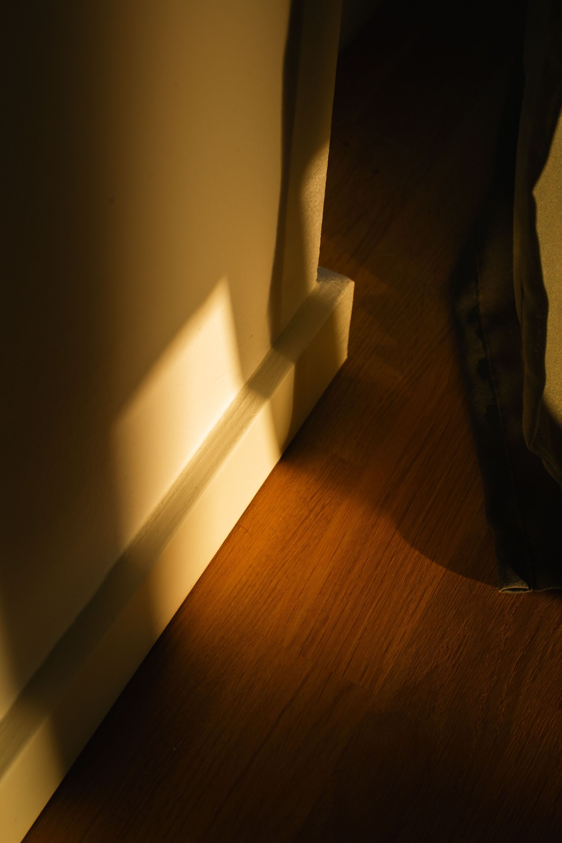 Sunlit hallway corner with a white wall, wooden floor, and a person standing at the edge of the frame