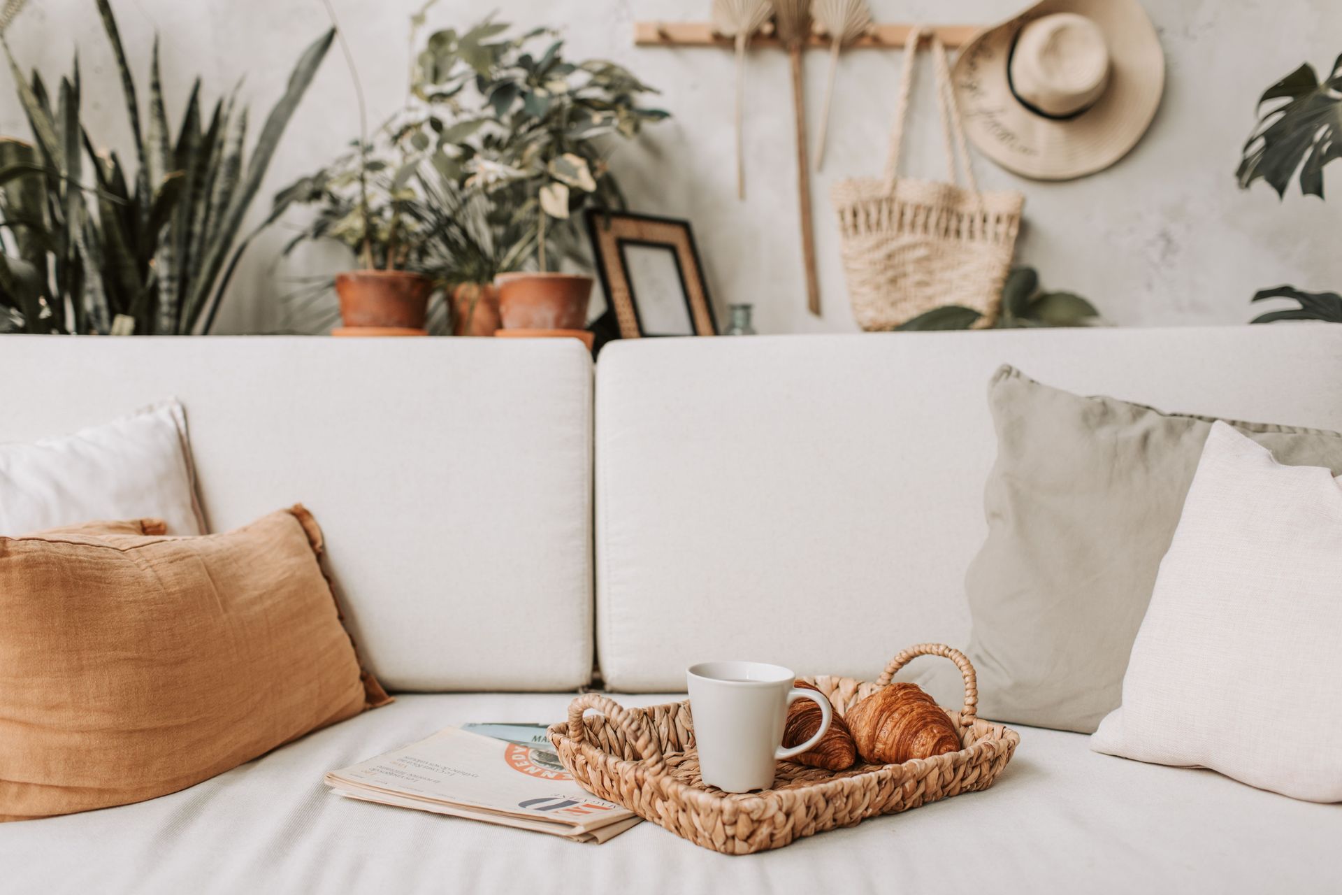 Cozy white sofa with tan pillows, tray of croissants and coffee, surrounded by houseplants and decor