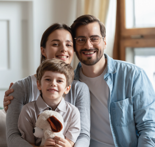 Family of three smiling, posing indoors. Child holds a stuffed animal.