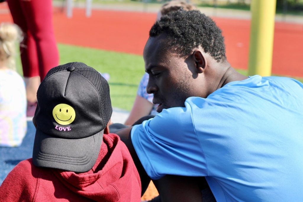 Man in blue shirt leans toward child in red hoodie and smiley face hat.