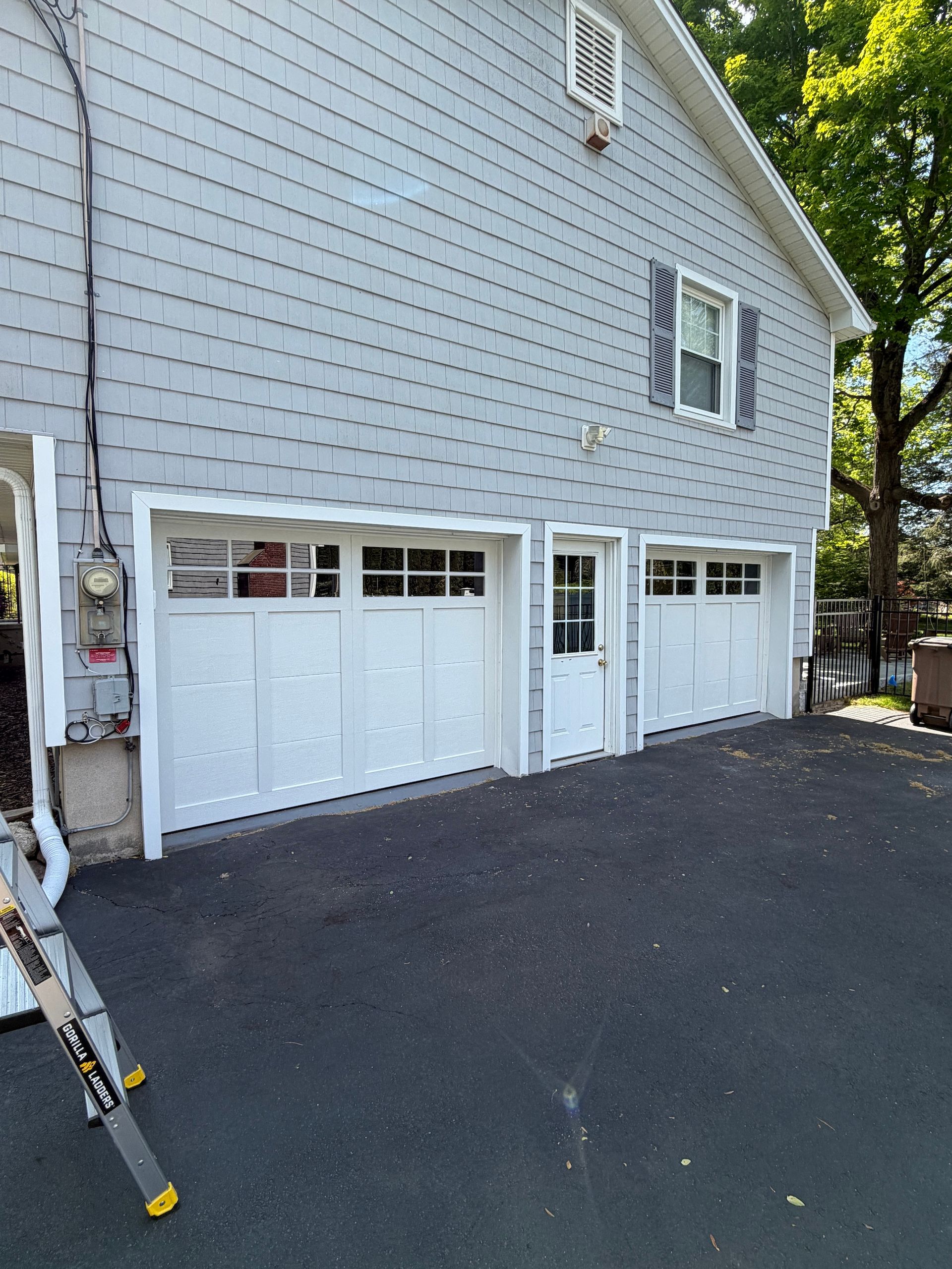 House exterior with white garage doors, gray siding, and black asphalt driveway