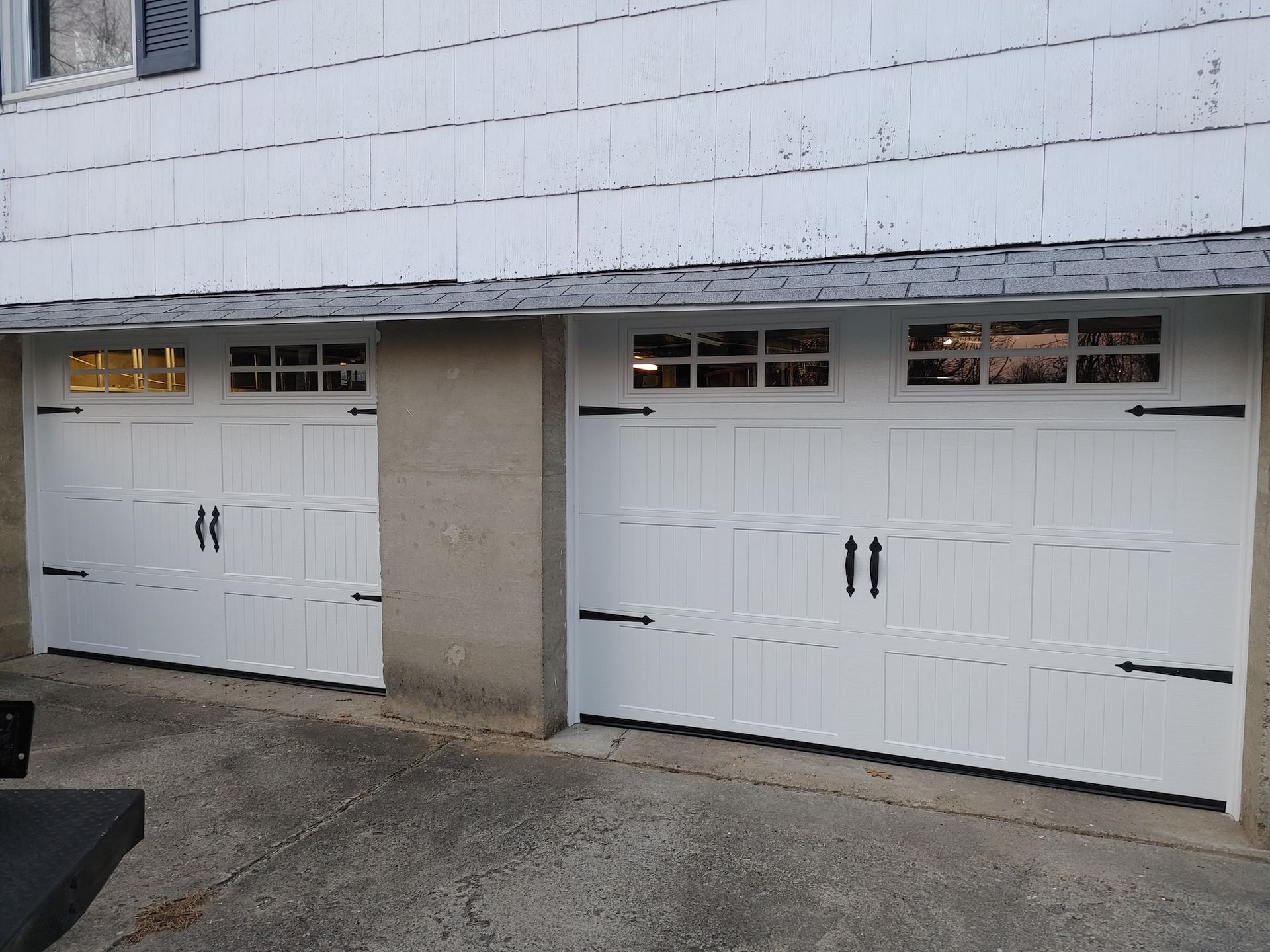 White double garage doors on a building exterior, with concrete driveway and small windows above each door