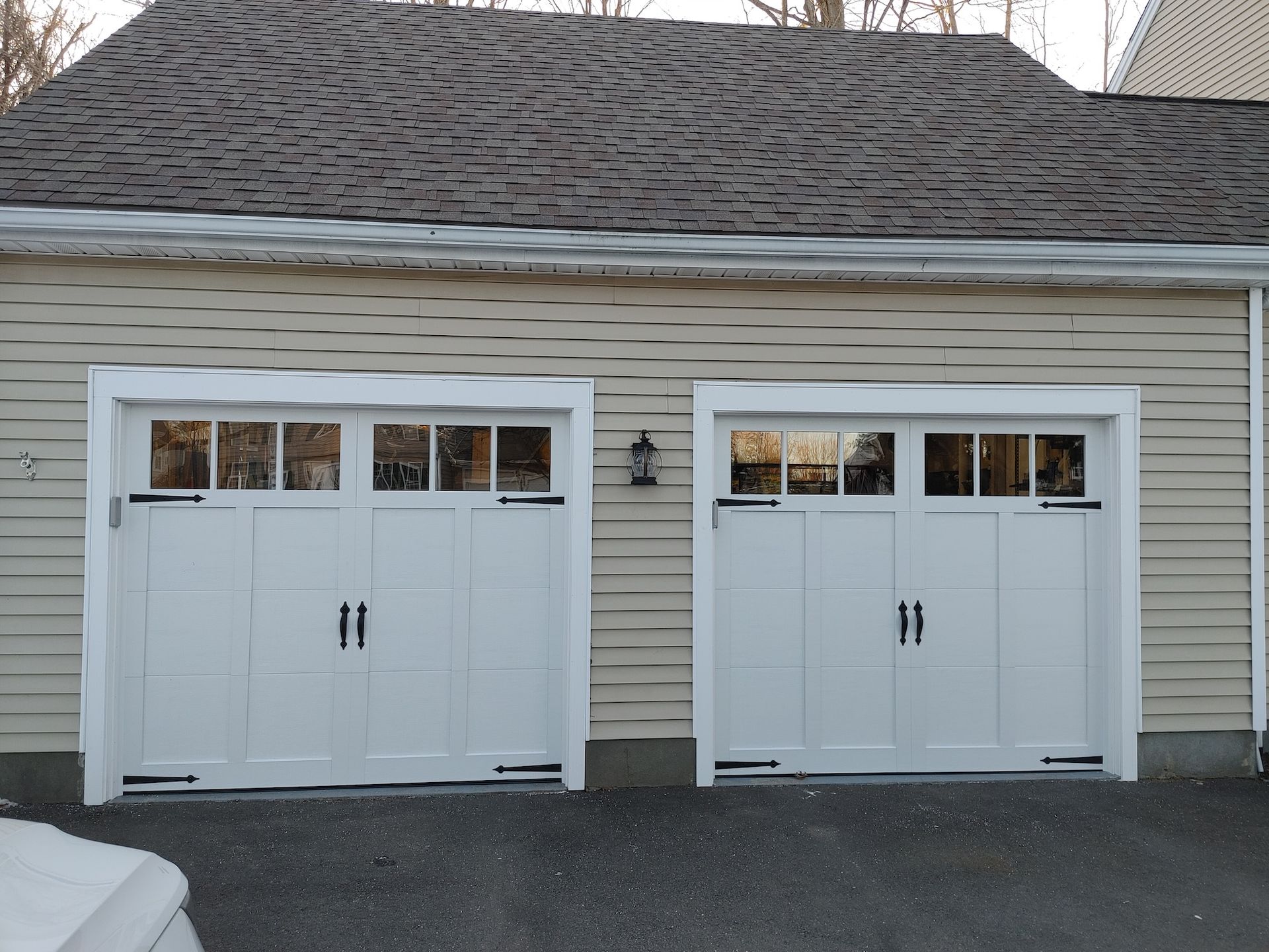 Two white garage doors on a beige house with gray shingled roof and asphalt driveway