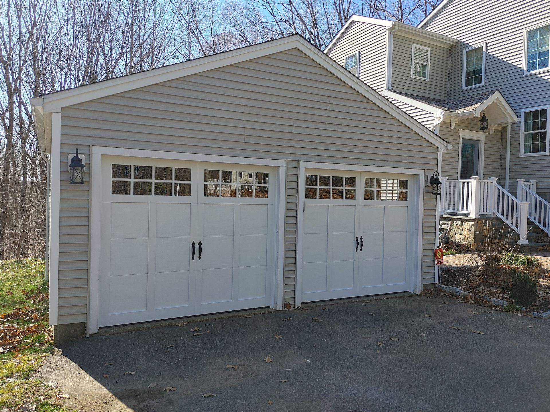 Two-car white garage with gabled roof and tan siding beside a house, seen from a driveway.