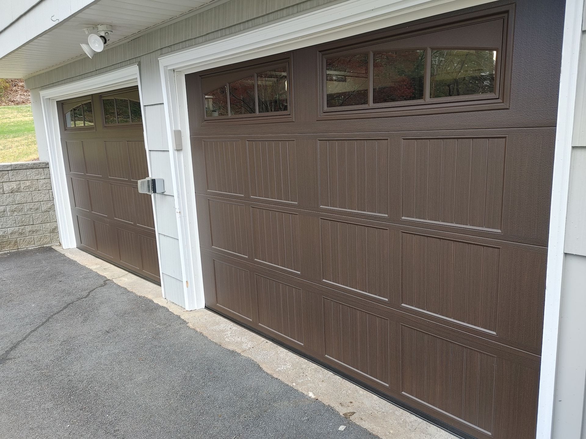 Two brown garage doors with white trim on a residential driveway