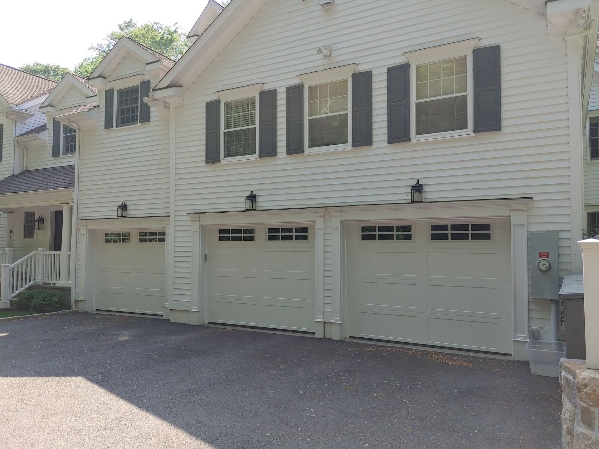 Row of white garage doors on a house with black shutters and a paved driveway