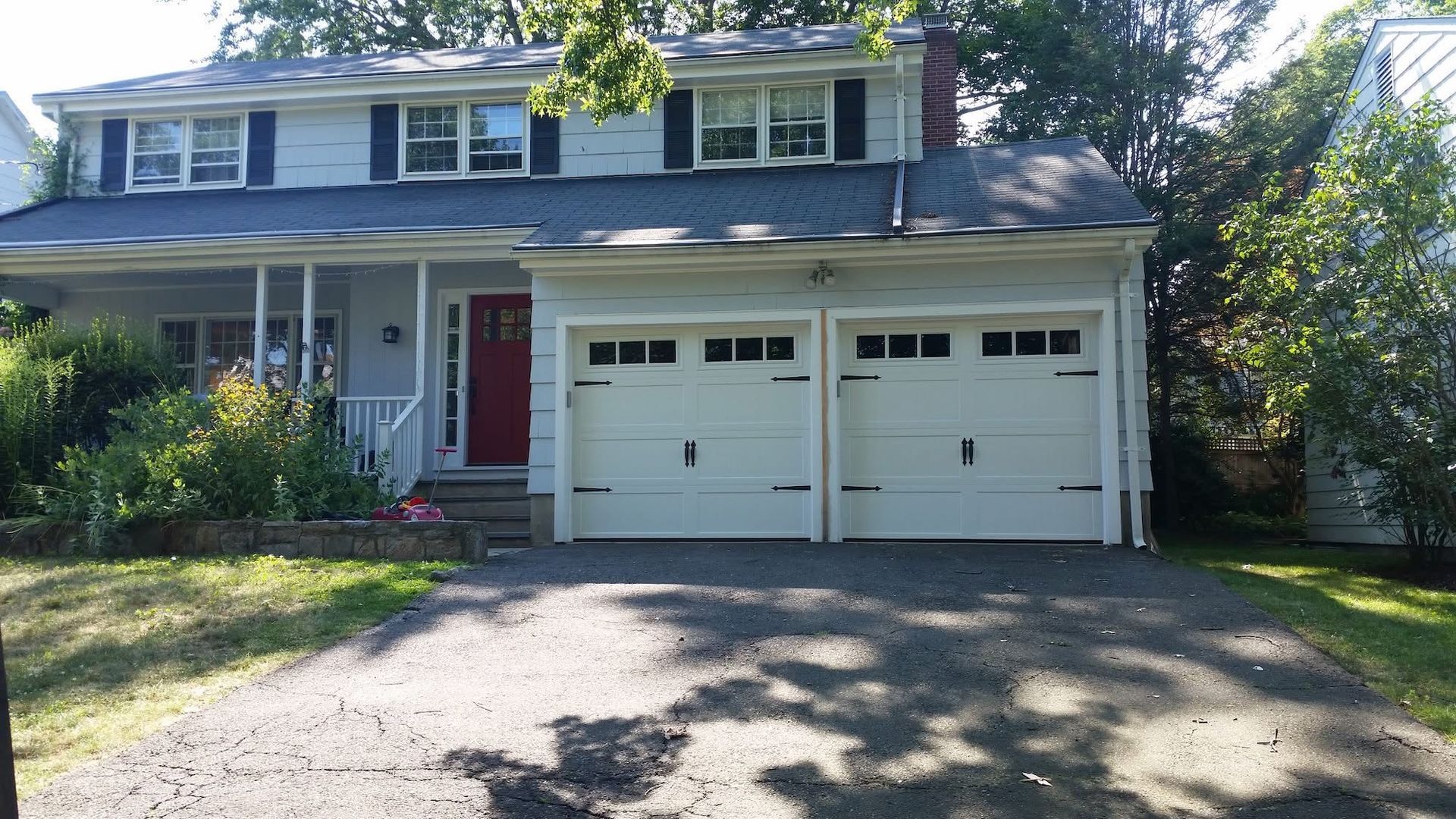 Suburban two-story house with a red front door and two-car garage, viewed from the driveway