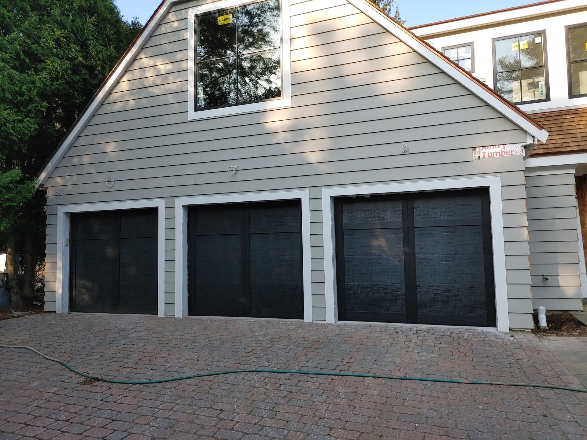 Three-car garage with beige siding and black doors on a brick driveway.