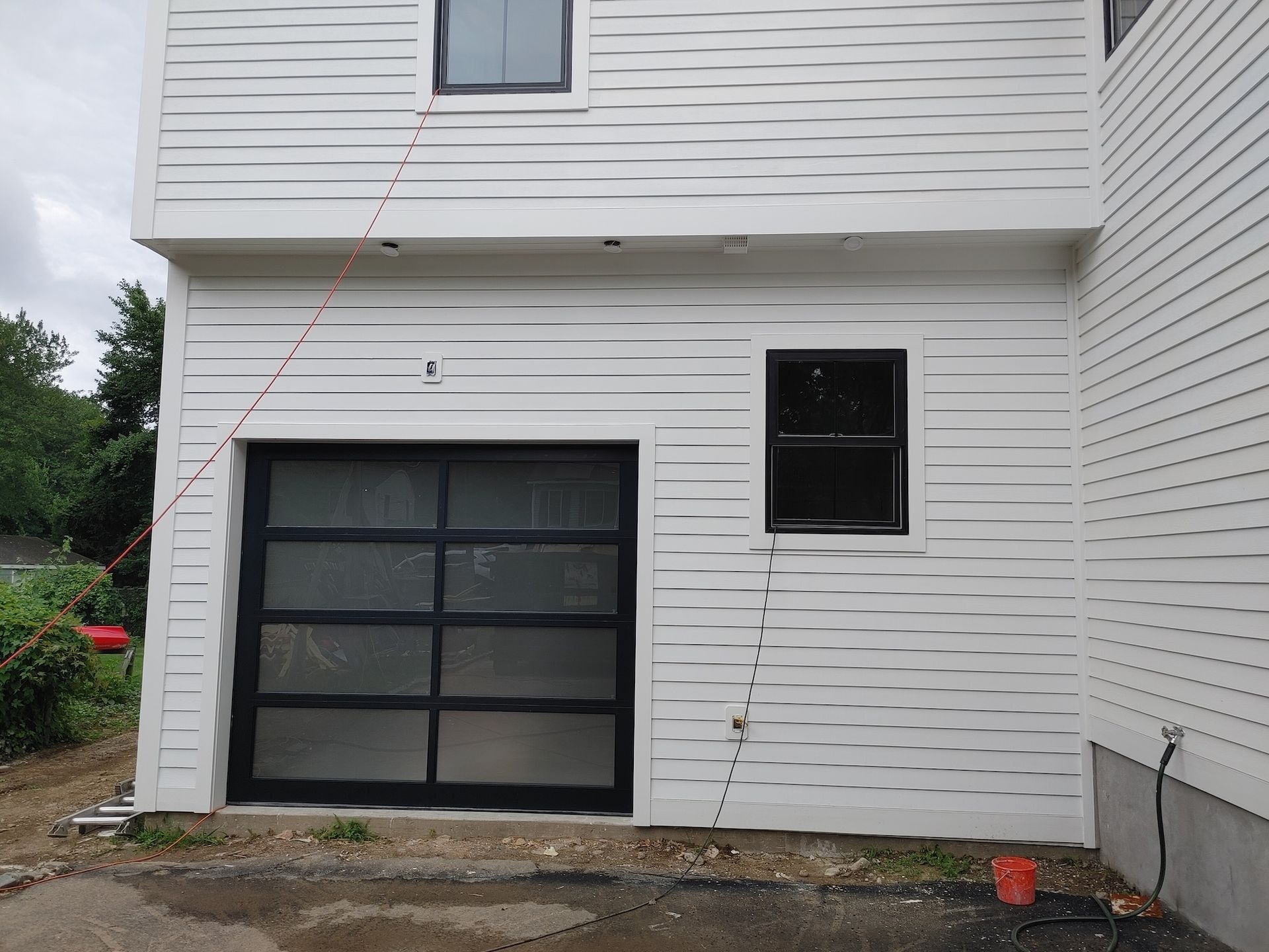 White house exterior with a black garage door and small window, showing a narrow side yard.