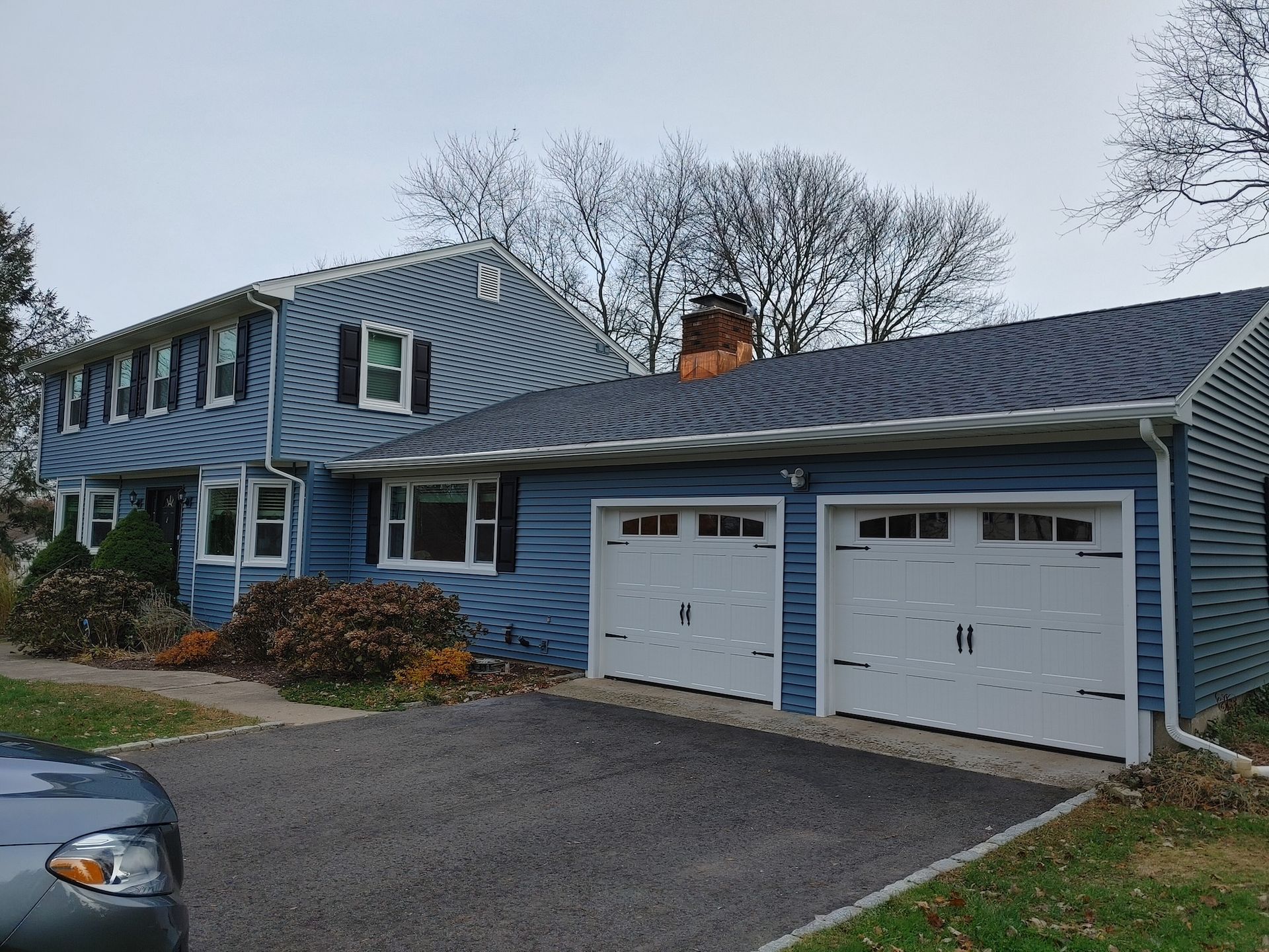 Blue two-story house with striped siding and two white garage doors on a cloudy day