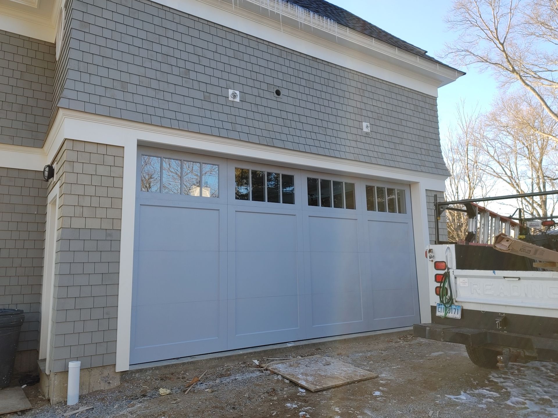 Light blue garage door on a gray house exterior with snow on the ground