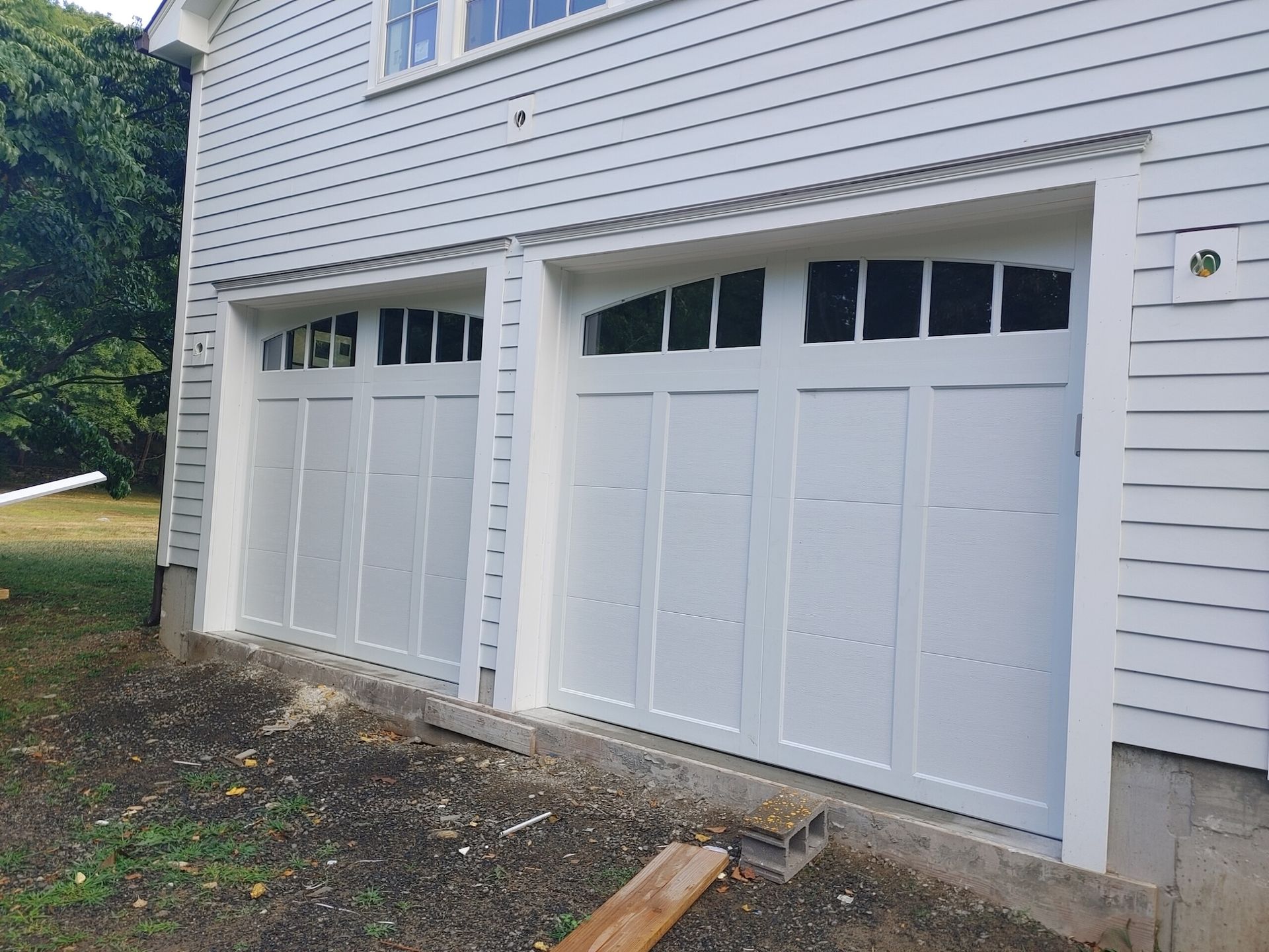 Two white garage doors on a house with light siding and a small concrete step.