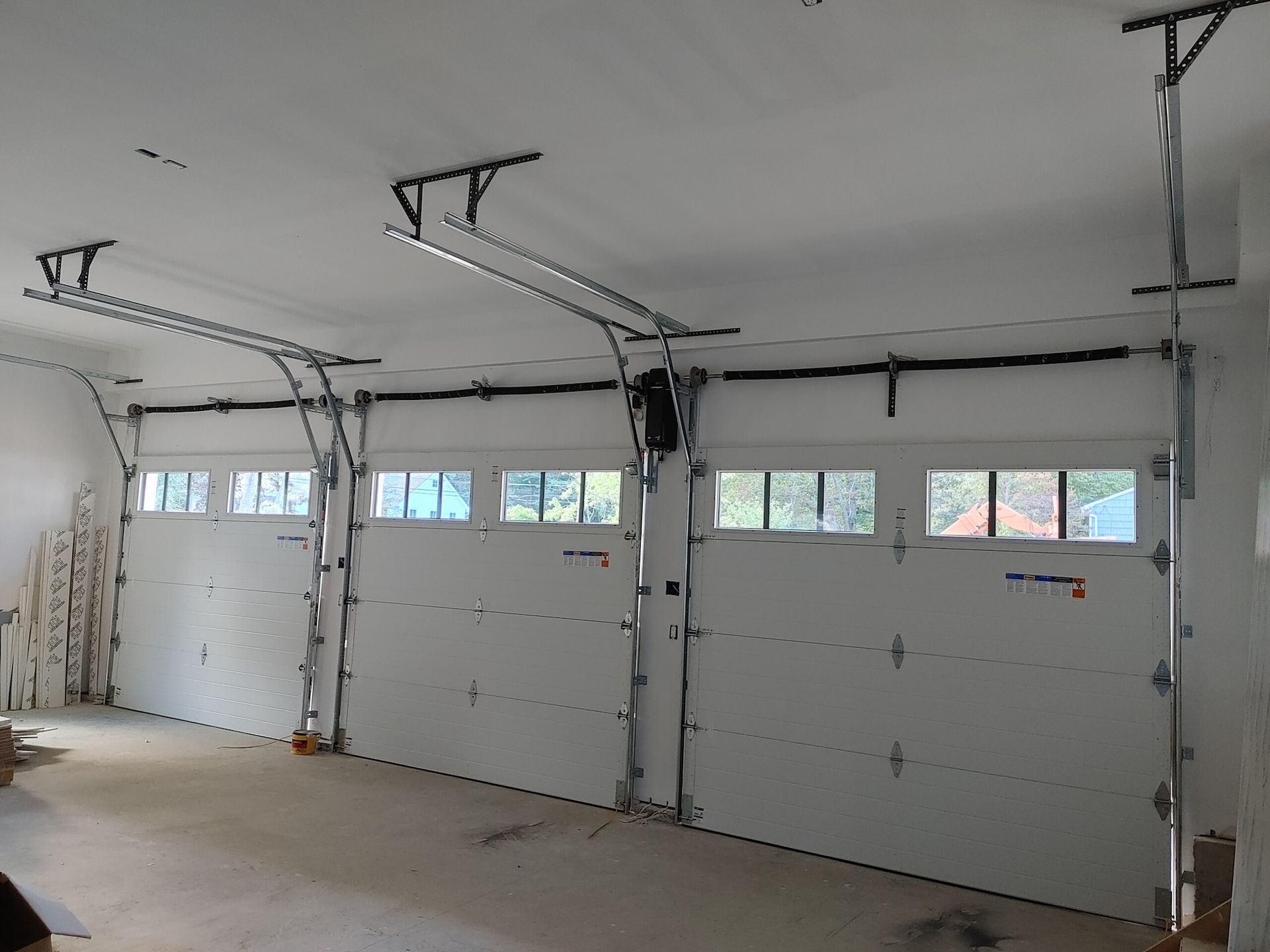 Interior of a garage with three white sectional doors and ceiling-mounted openers