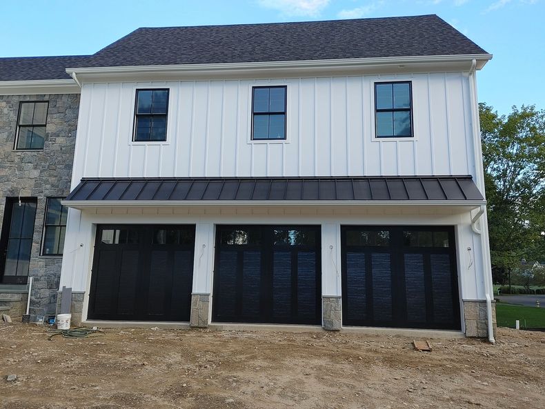 Two-story white house with stone side wall and three dark garage doors under construction