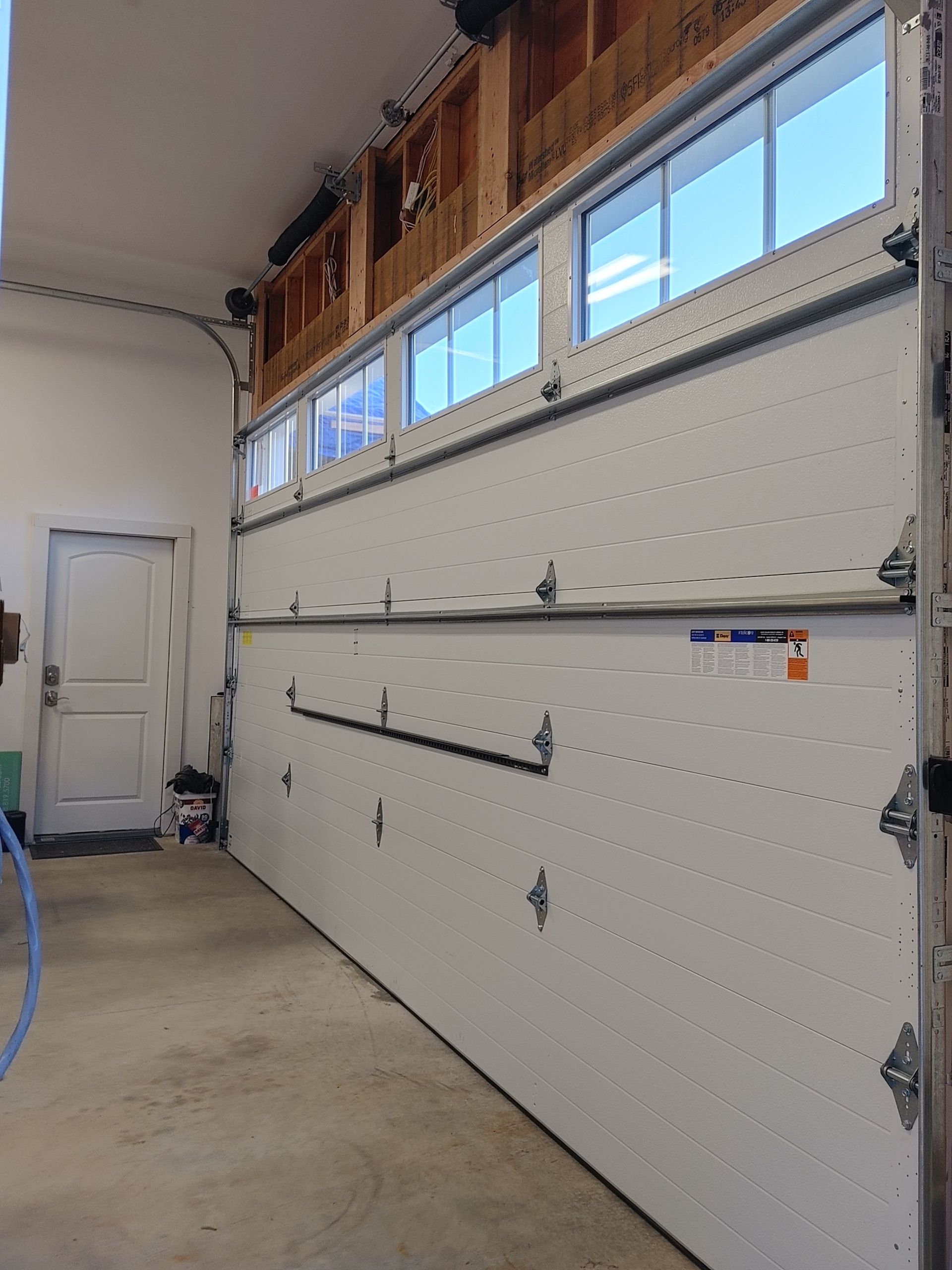 Interior of a garage with a white sectional overhead door, windows near the ceiling, and concrete floor.