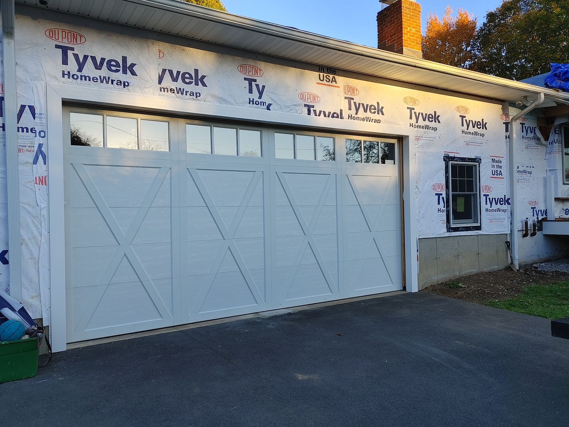 White garage door on a house with Tyvek house wrap and a small side entrance.