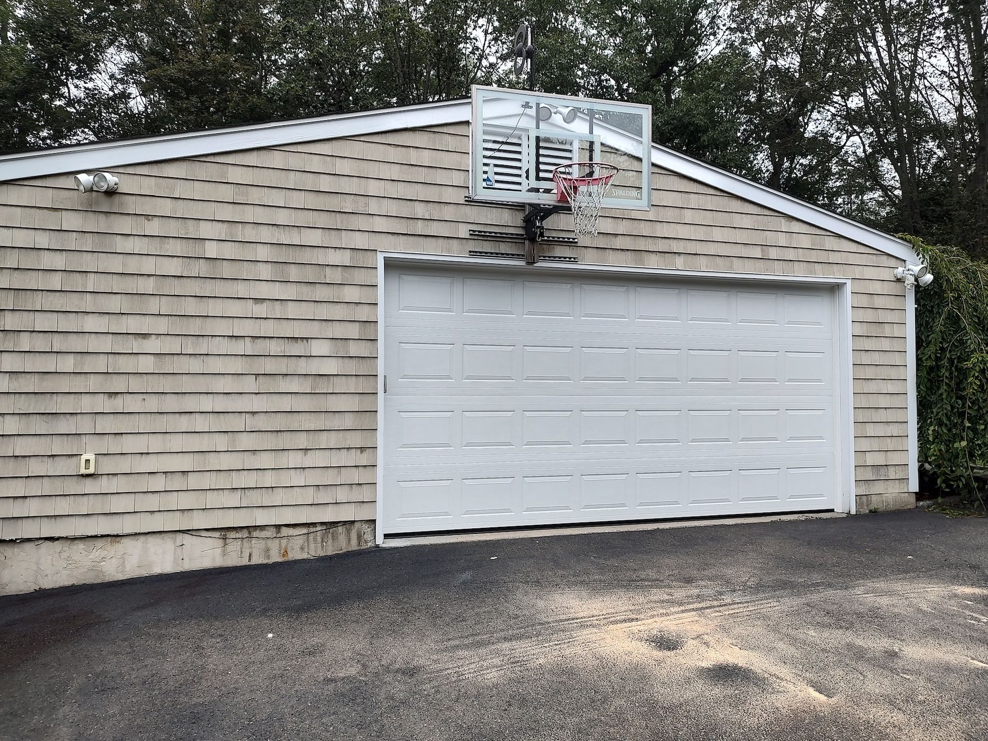 Detached garage with white door and mounted basketball hoop in a driveway.