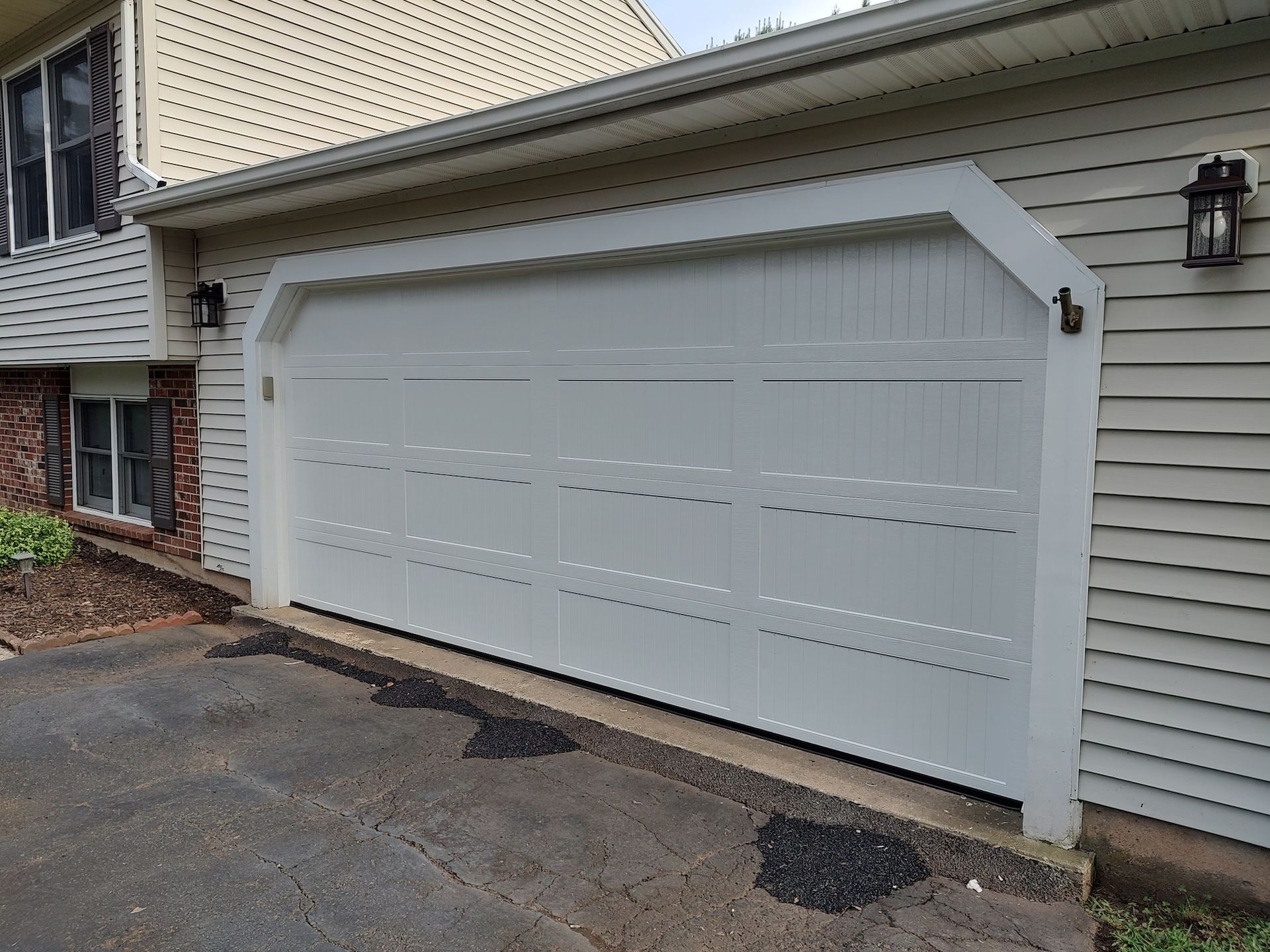 White double garage door on a beige house exterior, beside a driveway and stone wall.