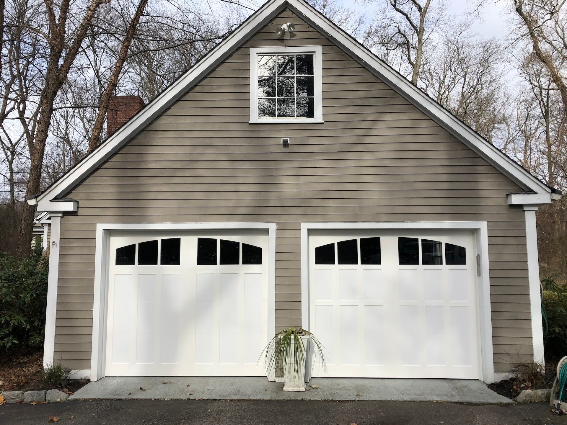 Gray two-car garage with white doors and a small window on top, surrounded by bare trees