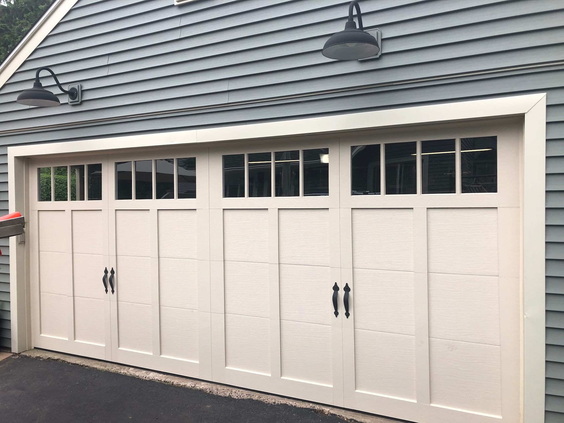 White garage doors with windows on a gray shingled house exterior