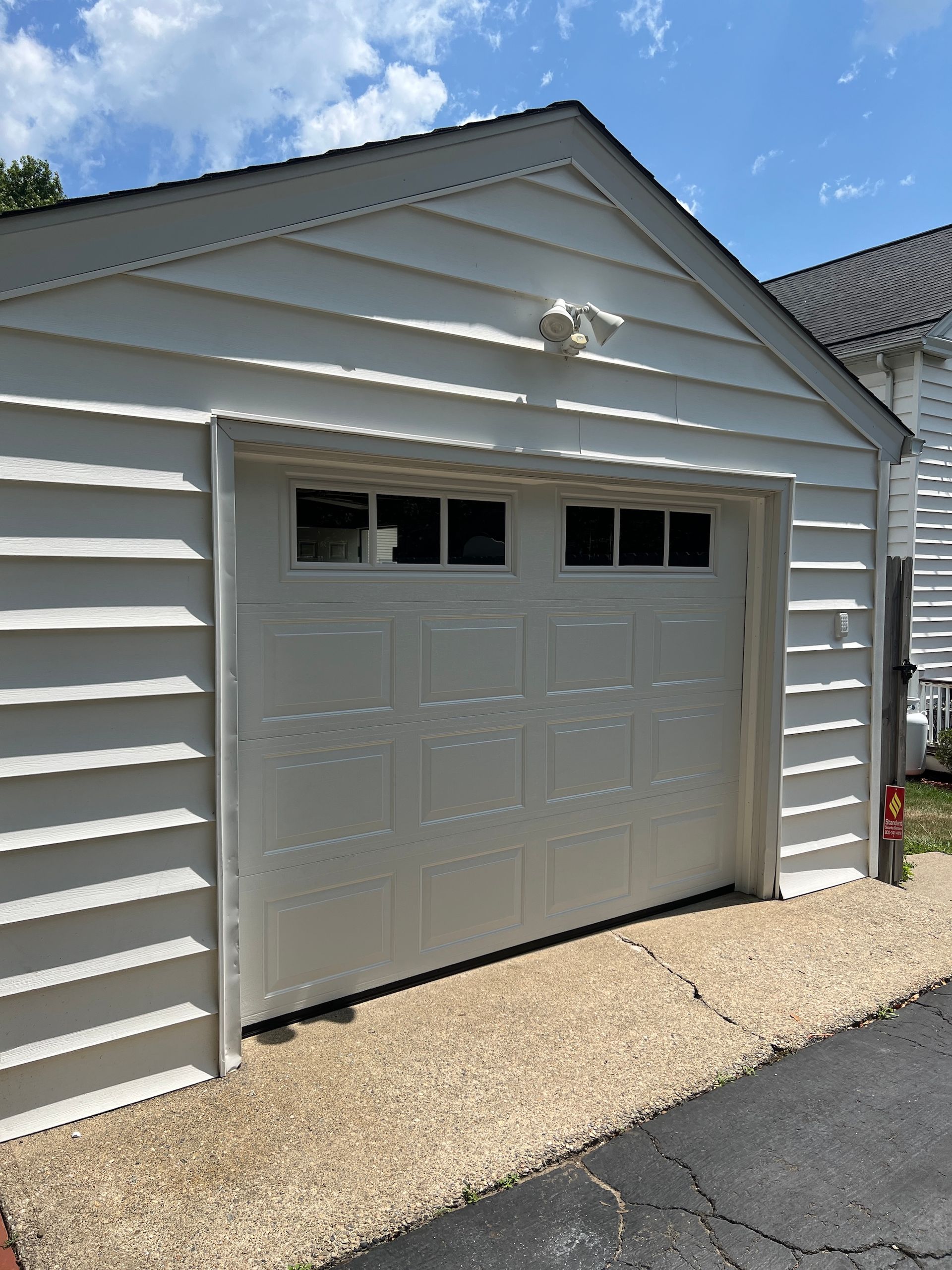 Gray garage door with four windows on a light-sided house, beside a gravel driveway under a blue sky
