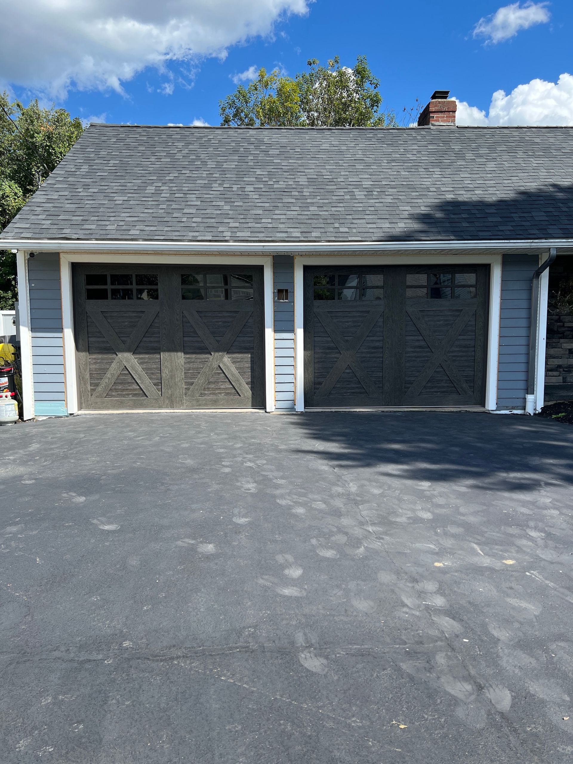 Two-car garage with gray shingle roof, white trim, and dark driveway under a blue sky.