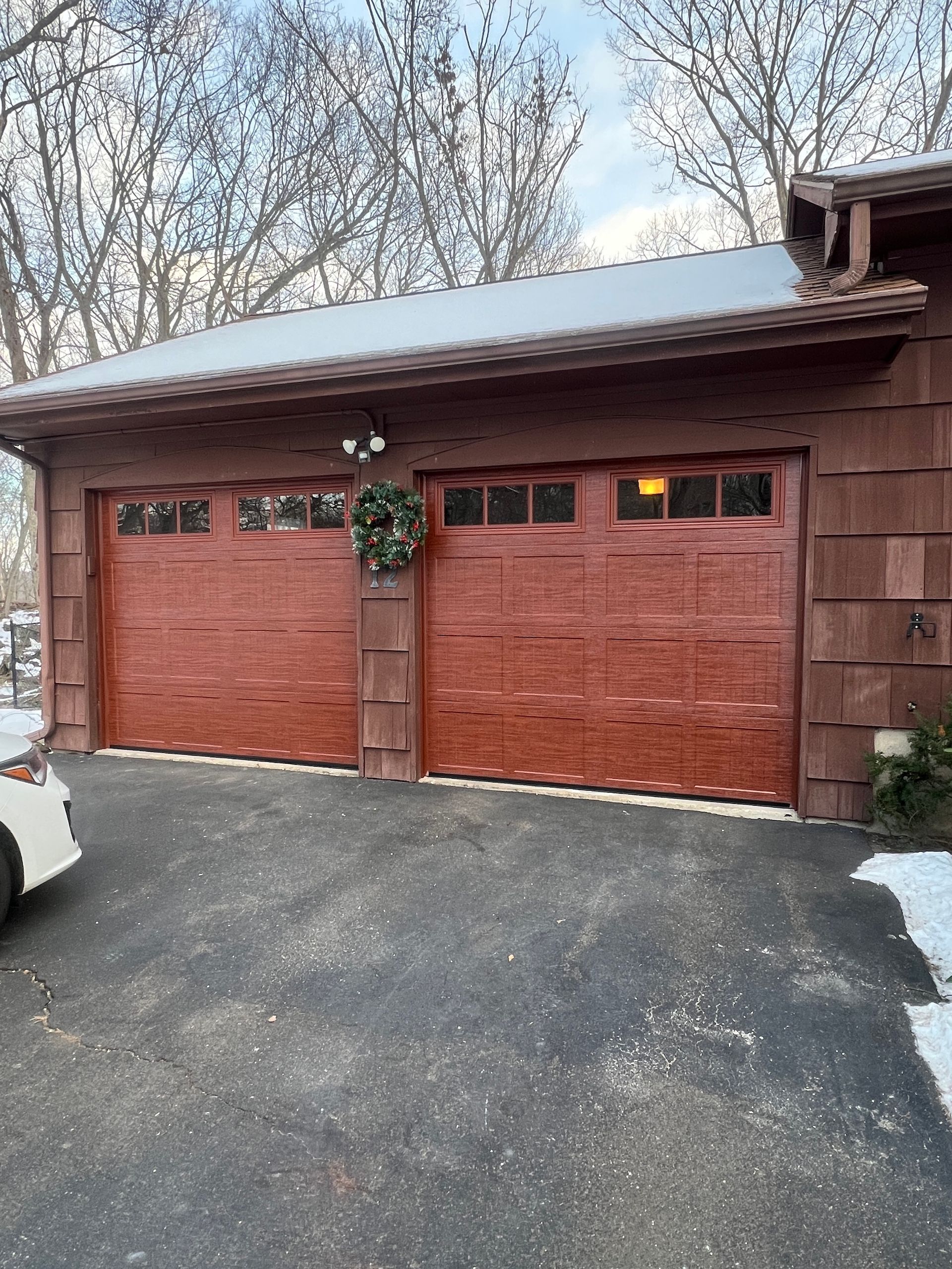 Two-car wooden garage with red doors, wreath, and snow on the roof and driveway.