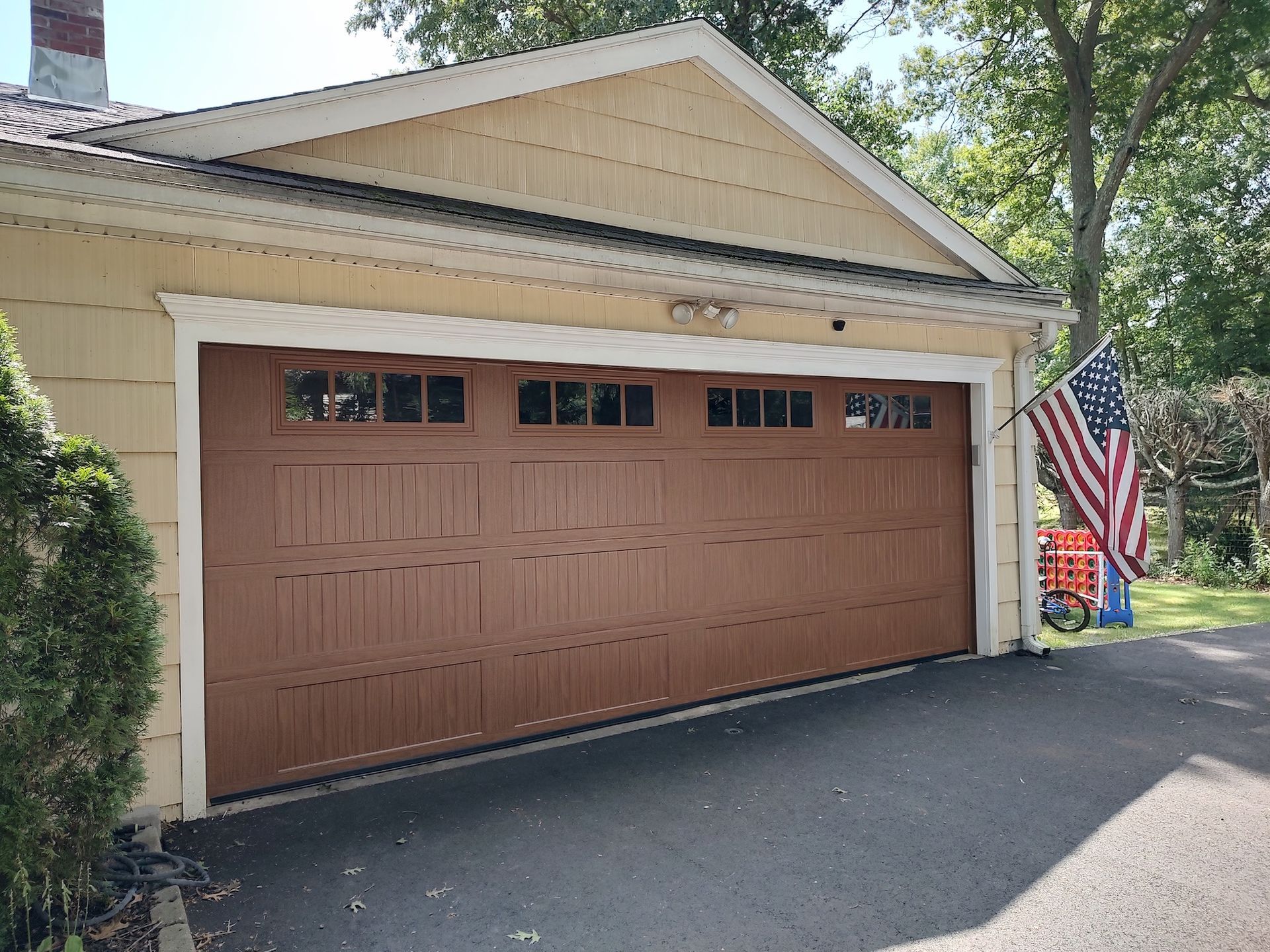Residential garage with a brown door, beige siding, and an American flag by the driveway