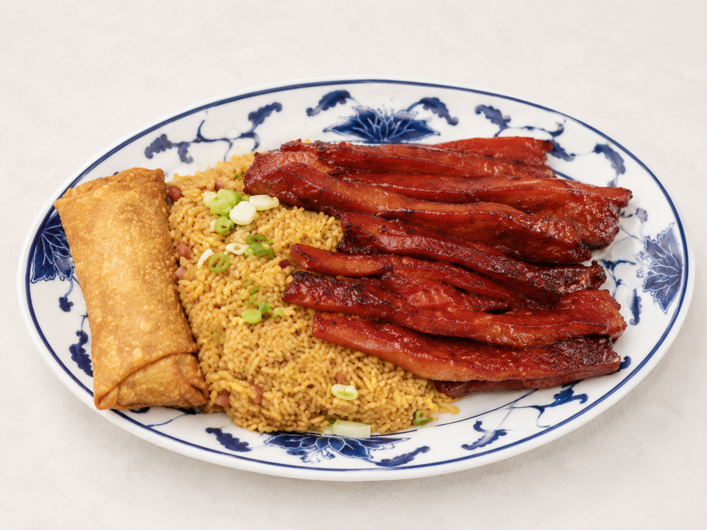 Plate of fried noodles with roasted red meat and a spring roll on a blue-and-white dish