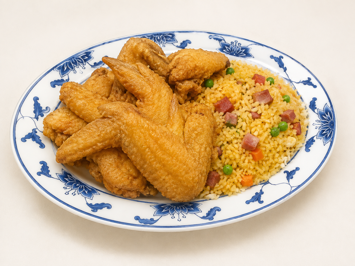 Plate of fried chicken wings with yellow rice and bits of sausage on a blue-and-white platter