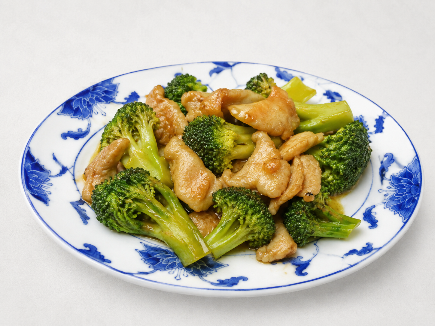 Blue-and-white plate of broccoli and chicken stir-fry on a white background