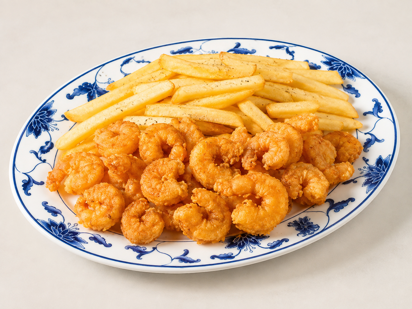 Plate of fried shrimp with French fries on a blue-and-white floral dish