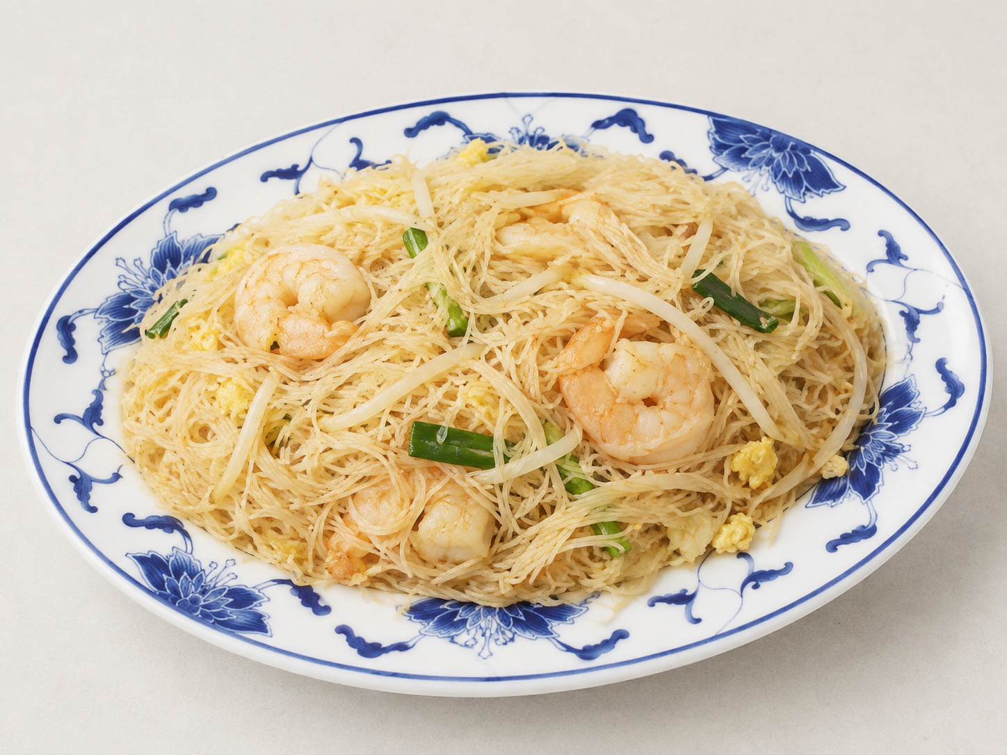 Shrimp stir-fried noodles on a white plate with blue floral rim